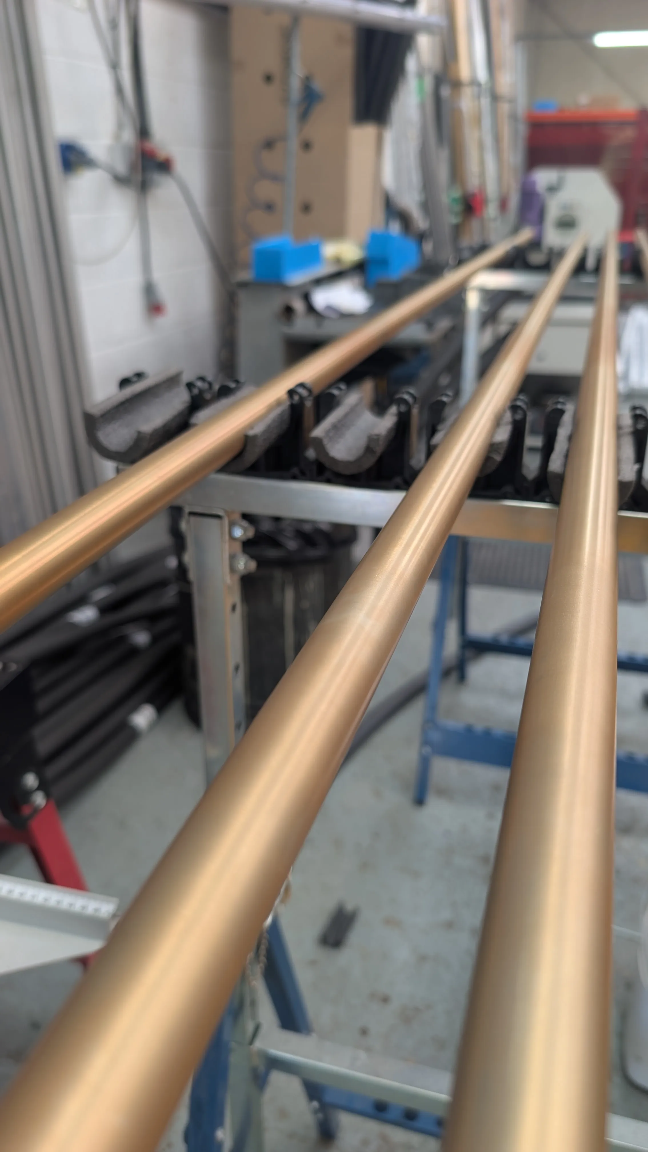 Long satin-polished, bronze-toned 1 inch element tubes lying on racks in the Solstrand workshop